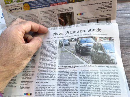 Foto de Kehl, Alemania - 29 de septiembre de 2023: Se ve una mano masculina sosteniendo una copia del periódico Kehler Zeitung. El titular informa que una hora de estacionamiento en la vecina Estrasburgo, Francia podría costar hasta 35 - Imagen libre de derechos