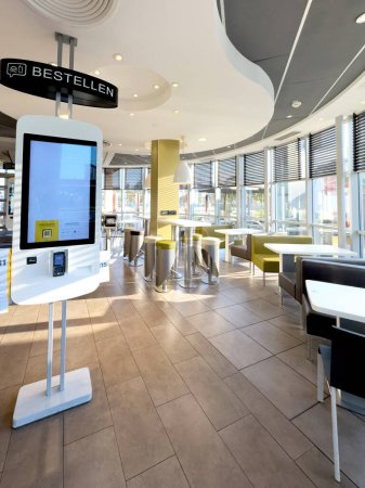 Foto de Kehl, Alemania - 29-sep-2023: Interior de un restaurante McDonalds vacío temprano en la mañana con mesas de bar, mesas normales y máquinas de autoservicio esperando a los clientes - Imagen libre de derechos