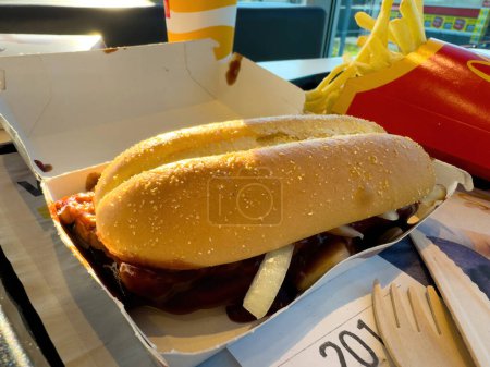 Téléchargez les photos : Kehl, Allemagne - 29 sept. 2023 : Une boîte ouverte avec un McRib, le sandwich au porc aromatisé barbecue, ainsi qu'un couteau et une fourchette en bois, sur une table à l'intérieur d'un restaurant McDonalds. Frites sont visibles - en image libre de droit