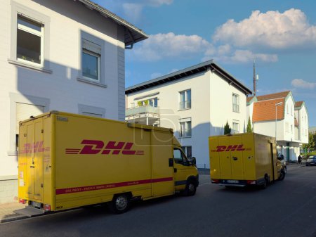 Photo for Kehl, Germany - Sep 29, 2023: Two yellow DHL delivery vans parked side by side in a city center, closely situated to nearby apartment buildings. - Royalty Free Image