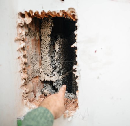 Foto de Una mano masculina es capturada dirigiendo la atención hacia una cavidad de la pared, un aspecto importante de las renovaciones en curso del horno para una estufa de leña. - Imagen libre de derechos