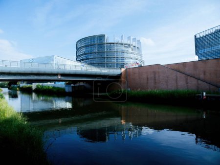 Téléchargez les photos : Une vue imprenable saisit le pont et le bâtiment du Parlement, flanqué d'un canal d'eau serein, avec les drapeaux de l'UE flottant gracieusement dans la brise. - en image libre de droit