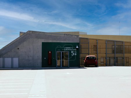 Photo for An isolated red car is parked on the left-hand side at the exit of a modern rooftop parking facility, emphasizing the spaces contemporary design - Royalty Free Image