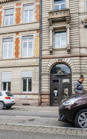 Téléchargez les photos : Strasbourg, France - 27 Ju 2023 : Une agente diligente vérifie les plaques d'immatriculation avant d "émettre une amende de stationnement avec un bâtiment en arrière-plan - en image libre de droit