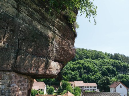 Foto de Surge la colosal casa de roca troglodita, su piedra que se mezcla sin esfuerzo con el bosque cercano y el encantador pueblo de Graufthal, Eschbourg, Bas-Rhin, Alsacia - Imagen libre de derechos