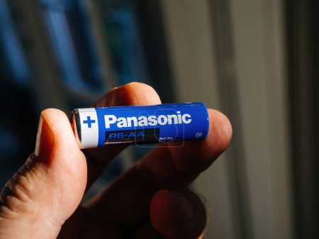 Foto de Lyon, Francia - 6 de septiembre de 2023: se ve una mano masculina sosteniendo una batería azul Panasonic R6-AA, claramente exhibida contra un fondo deliberadamente desenfocado - Imagen libre de derechos