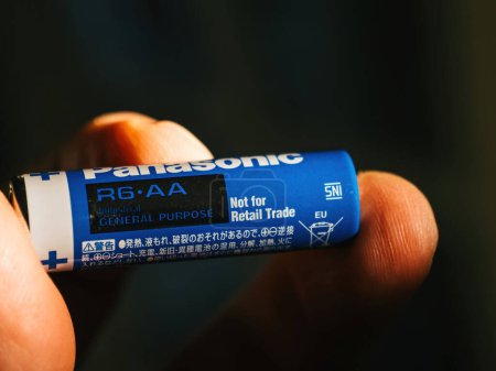 Photo for Lyon, France - Sep 6, 2023: a male hand is seen gripping a Panasonic R6-AA general-purpose industrial alkaline battery, marked with a Not for Retail Trade sign. - Royalty Free Image