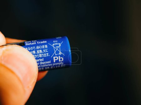 Foto de Lyon, Francia - 6 de septiembre de 2023: una mano masculina sostiene una batería Panasonic AA de color azul, que destaca por presentar un letrero que no contiene Pb, colocado sobre un fondo negro desenfocado. - Imagen libre de derechos