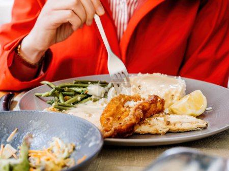 Téléchargez les photos : Femme en manteau rouge mangeant de délicieux poissons au citron et riz à l'aide d'une fourchette, sur une terrasse extérieure d'un restaurant - en image libre de droit