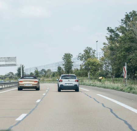 Téléchargez les photos : France- 17 août 2023 : Vue arrière carrée d'une Bentley de luxe et d'une Citroën C3 modeste coexistant sur une autoroute française, saisissant la diversité des goûts automobiles. - en image libre de droit