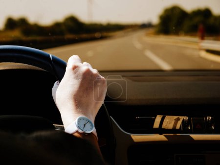 Photo for A woman wearing an elegant timepiece watch on her wrist, driving along a solitary road with an uncertain destination and serene outdoor scenery - Royalty Free Image