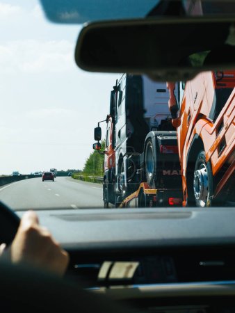 Téléchargez les photos : France- 17 août 2023 : Perspective de l'intérieur d'un véhicule passant par une remorque cargo transportant plusieurs camions MAN le long de l'autoroute. - en image libre de droit