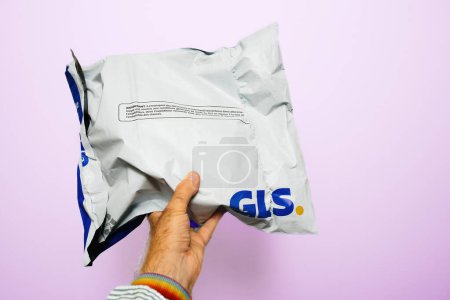 Photo for Paris, France - Sep 6, 2023: A male hand firmly grips a GLS parcel against a clean white-pink backdrop - Royalty Free Image