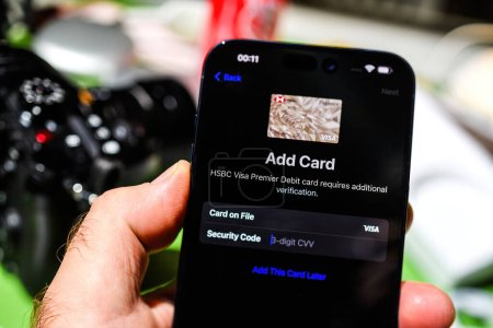 Photo for London, UK - Sep 28, 2023: A tilt-shift lens captures a hand holding the iPhone 15 Pro Max, setting up an HSBC Premiere card in Apple Pay, ensuring secure card verification - Royalty Free Image