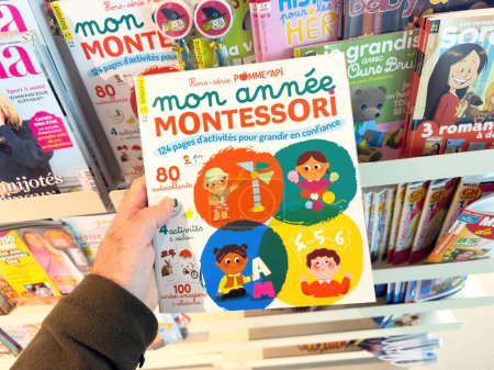 Foto de París, Francia - 10 de octubre de 2023: Mano masculina sosteniendo Mis años Montessori en francés por Pomme dApi Editions en el quiosco de prensa. Explora grandes lecturas para niños y niños pequeños - Imagen libre de derechos