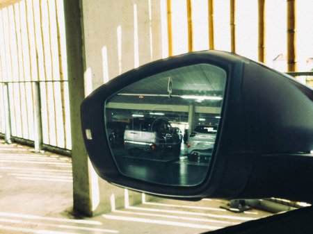 Téléchargez les photos : Dans un parking couvert, le rétroviseur affiche une vue sur de nombreuses voitures stationnées, mettant en valeur l'aire de stationnement organisée. - en image libre de droit