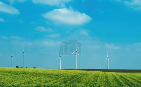 Foto de Campo de colza idílico, paisaje de color amarillo con múltiples molinos de viento que generan electricidad y un cielo azul claro en el fondo: una imagen de planificación de la vida urbana ecológica - Imagen libre de derechos