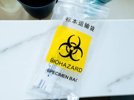 Foto de Cartel amarillo de riesgo biológico en una bolsa de plástico con texto de muestra en inglés y chino, sometido a la prueba COVID-19 en casa - Imagen libre de derechos