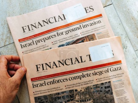 Photo for Paris, France - Oct 11, 2023: Male hand holding two editions of Financial Times newspaper with headline Israel Prepares for Ground Invasion and Enforcing Complete Siege of Gaza - Royalty Free Image