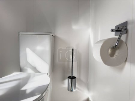 Foto de Baño moderno con soporte de papel higiénico cromado pulido, cepillo e inodoro de porcelana - Imagen libre de derechos