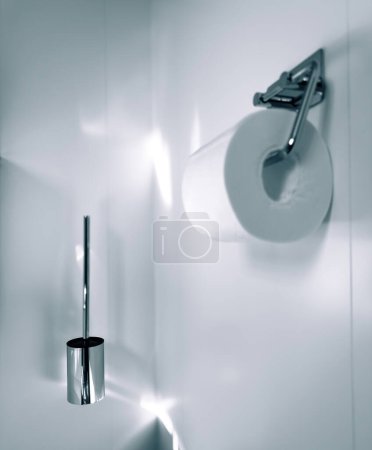 Téléchargez les photos : Dans une salle de bain moderne de luxe, un porte-papier toilette argenté avec un rouleau et une brosse de toilette chromée sont élégamment montés sur le mur carrelé - en image libre de droit