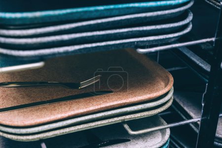 Photo for A stack of multiple lunch tray plates in brown, blue, and sand colors, with a fork and knife between them. Suitable for canteens, schools, offices, and corporations - Royalty Free Image
