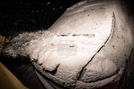 Photo for Fast-motion capture of a man vigorously clearing snow off a car or truck, focusing on the rear window, during a snowstorm - striking exterior flash photography - Royalty Free Image