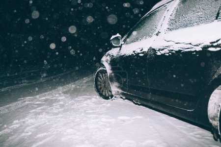 Téléchargez les photos : Voiture conduisant la nuit lors d'une tempête de neige, entourée d'une rafale de flocons de neige, se dirigeant vers l'inconnu - en image libre de droit