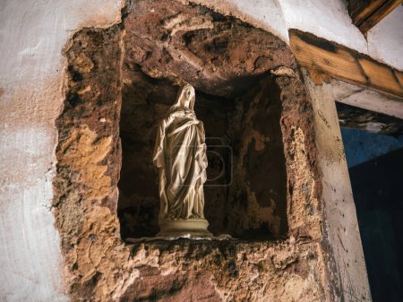 Téléchargez les photos : Dans le coin tranquille d'une demeure troglodyte, une vieille statue de Marie se tient dans une prière fervente, incarnant un poignant symbole de foi et un appel sincère à la paix. - en image libre de droit