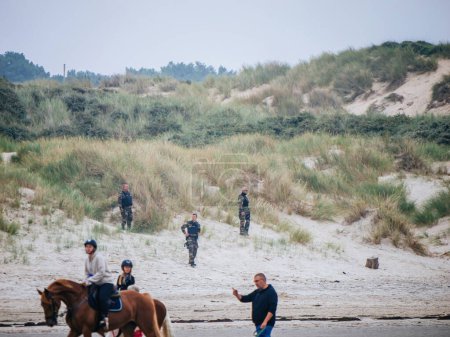 Foto de Neufchatel-Hardelot, Francia - 18 / 08 / 2023: Los asistentes a la playa disfrutan de la equitación, mientras que la policía y los oficiales militares patrullan las dunas en busca de migrantes - Imagen libre de derechos