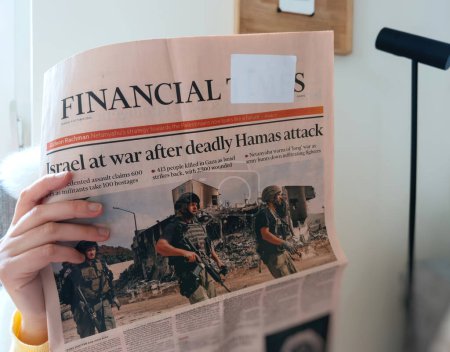 Téléchargez les photos : Paris, France - 10 oct. 2023 : Le salon offre une toile de fond tranquille alors qu'une femme lit le dernier journal du Financial Times intitulé Israël en guerre après l'attaque meurtrière du Hamas. - en image libre de droit