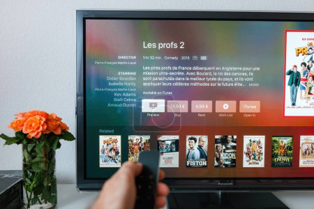 Foto de París, Francia - 25 de noviembre de 2015: Una mano masculina apunta el control remoto del Apple TV hacia un televisor de plasma 4K en la sala de estar, con menos brillo en la pantalla, mientras que un jarrón de rosas se sienta cerca - Imagen libre de derechos