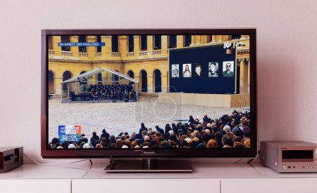 Photo for Paris, France - Nov 25, 2015: In a living room, a plasma television set is seen streaming the special edition of the Live Event Morning Memories for the Bataclan terrorist attacks in France, paying - Royalty Free Image