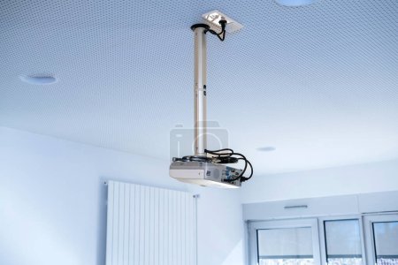 Photo for A blue-hued projector inside an office interior, mounted on a steel pole suspended from the ceiling - Royalty Free Image