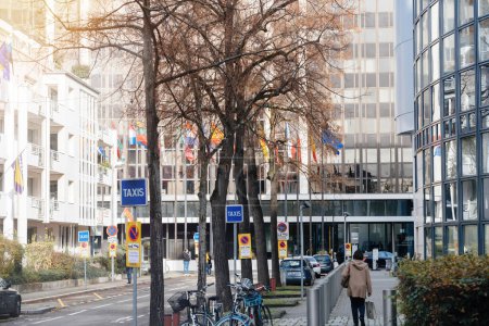 Téléchargez les photos : Strasbourg, France - 22 nov. 2023 : Un panneau de taxi se dresse bien en vue le long de la rue, avec le bâtiment Winston Churchill du Parlement européen en arrière-plan. Une femme piétonne peut être vue - en image libre de droit