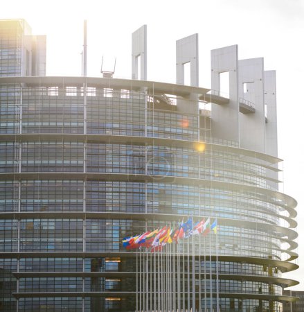 Photo for The European Parliament bathed in the soft glow of sunlight flare, with the flags of all EU member countries waving in the early morning breeze. Dominantly displayed is the Ukrainian flag, symbolizing - Royalty Free Image