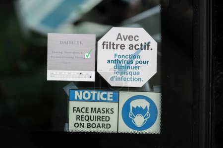 Foto de Estrasburgo, Francia - 22-nov-2023: Una ventana de autobús de autocar muestra varios avisos, incluyendo una tarjeta de verificación Daimler HVAC, un signo de requisito de máscara facial y una etiqueta de filtro antivirus activa en francés - Imagen libre de derechos
