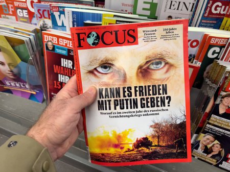 Téléchargez les photos : Francfort, Allemagne - 24 février 2023 : Une main saisit un magazine FOCUS montrant un gros plan d'un œil et un titre sur Vladimir Poutine sur fond de feu. Le porte-revues derrière révèle - en image libre de droit