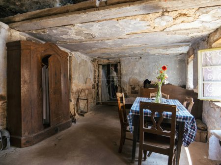 Foto de Una vista interior captura el ambiente de una casa troglodita con una mesa, sillas y una cama, con una ventana abierta, que proporciona una visión de las condiciones de vida antiguas - Imagen libre de derechos