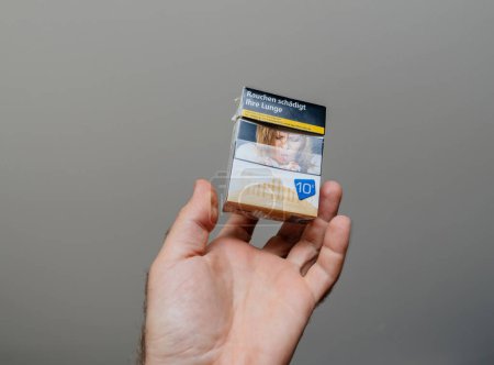 Foto de París, Francia - 30 de mayo de 2023: La mano masculina sostiene un paquete de cigarrillos Marlboro Gold, con texto alemán que enfatiza los riesgos para la salud de fumar, con una imagen que representa a una mujer que sufre de cáncer - Imagen libre de derechos