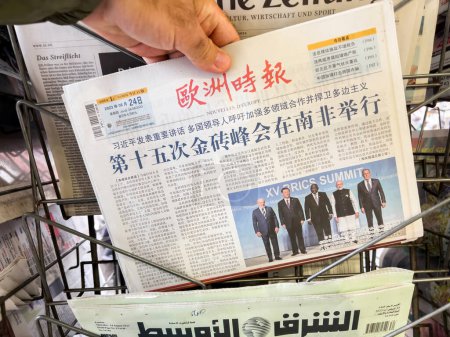 Téléchargez les photos : Paris, France - 26 août 2023 : Une main masculine tient le journal chinois European Times, avec des photos de participants chinois, indiens, africains et russes au XVe Sommet des BRICS - un précieux - en image libre de droit