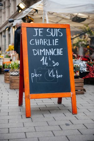 Téléchargez les photos : Un tableau sur la rue affiche bien en évidence la phrase Je Suis Charlie, indiquant un événement le dimanche à 14 : 30 à la Place Kleber, avec une toile de fond d'un étal de marché - en image libre de droit