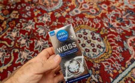 Téléchargez les photos : Paris, France - 1 Sep 2023 : Homme tenant le tube de dentifrice blanchissant Perl Weiss sur le tapis du salon - en image libre de droit