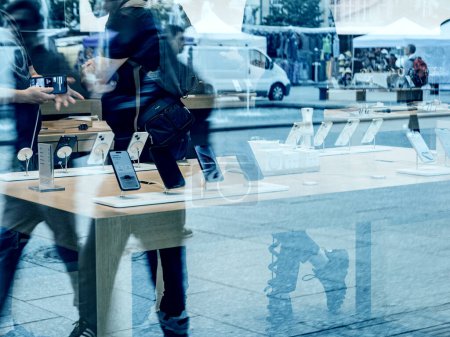 Foto de París, Francia - 22-sep-2023: Las siluetas de los peatones se reflejan en el cristal de una Apple Store ya que un Apple Genius ayuda a un cliente a comprar el iPhone 15 Pro Max - Imagen libre de derechos