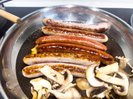 Photo for Six appetizing sausages fry alongside fresh white mushrooms in a pan, emanating a mouthwatering aroma and promising a delectable culinary experience - Royalty Free Image