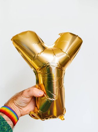 Foto de Primer plano de una mano masculina sosteniendo la letra Y hecha de un globo de helio inflable de oro. Aislado sobre un fondo blanco, ideal para varias ocasiones festivas - Imagen libre de derechos
