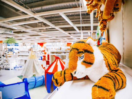 Un jouet de tigre en peluche sort d'une grande boîte dans un magasin de meubles pour enfants, avec une charmante tente de tipi installée derrière, au milieu d'une richesse de jouets et d'articles de maison