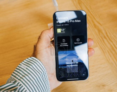 Foto de París, Francia - 22-sep-2023: Una mano masculina presenta el nuevo iPhone 15 Pro Max de Apple Computers, con un precio especial de 1470 euros, colocado sobre una mesa de madera rústica - Imagen libre de derechos