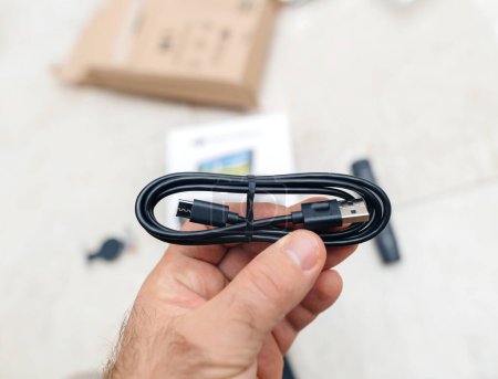 Foto de Vea una mano masculina sosteniendo cables USB y USB-C por encima de un unboxing de un paquete tecnológico, mostrando opciones de conectividad - Imagen libre de derechos