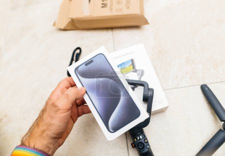 Téléchargez les photos : Paris, France - 24 oct. 2023 : une main masculine tenant la nouvelle boîte iPhone 15 Pro Max au-dessus d'une cartouche Osmo Mobile 6, livrée via Amazon Prime - colis carton en arrière-plan - en image libre de droit